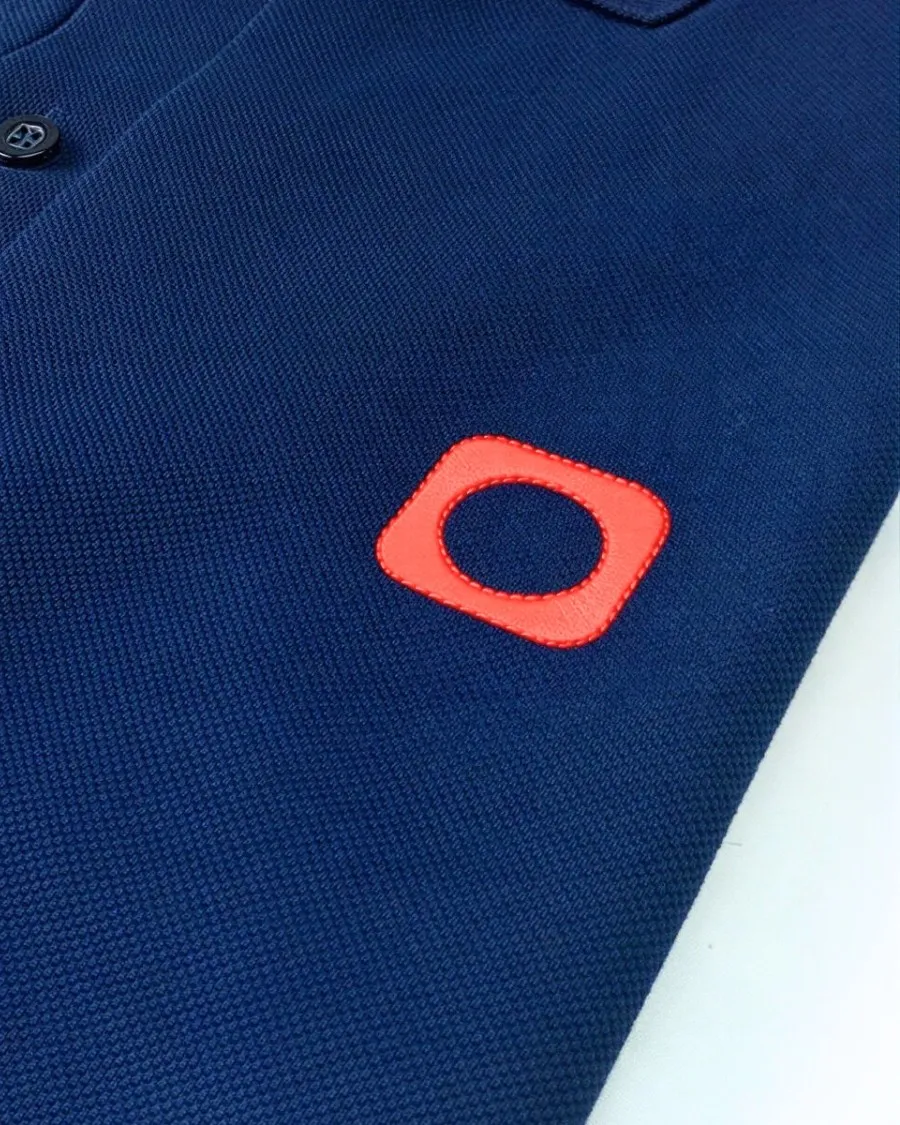 Close do logo laranja aplicado no peito de uma polo azul-marinho